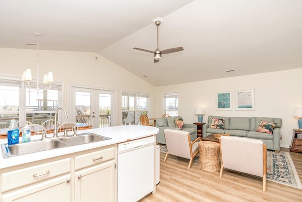 A spacious living area with a kitchen, a ceiling fan, and a sofa with cushions.