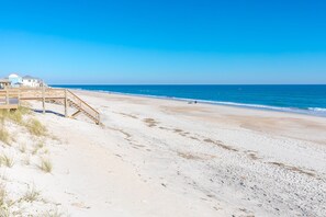 A beach with a wooden staircase leading to a building, clear skies, and calm sea.