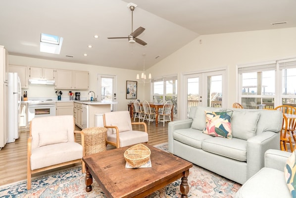 A spacious living room with a sofa, chairs, a coffee table, and a kitchen in the background.