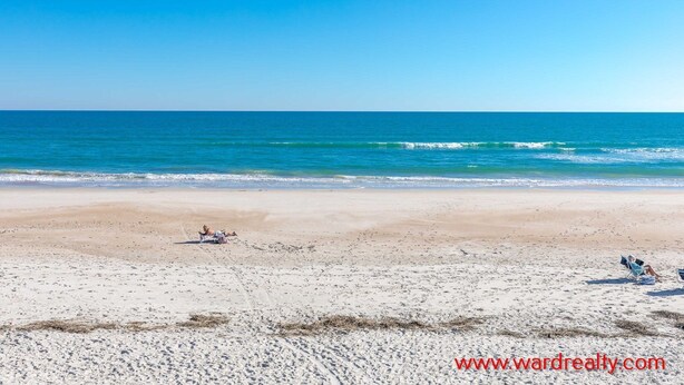 A beach with a clear sky, calm sea, and footprints in the sand.