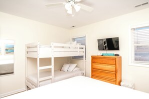 A bunk bed room with a ceiling fan, a television, and a wooden dresser.