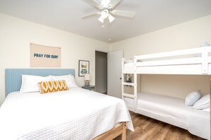 A bedroom with a bed, a bunk bed, a ceiling fan, a bedside table, and a wall with a poster.