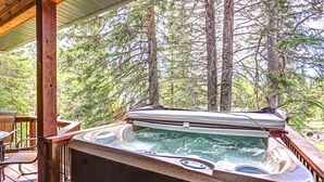 A hot tub on a wooden deck with a view of tall trees.