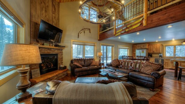A spacious living room with a fireplace, leather sofas, and a television. A wooden staircase leads to an upper level.