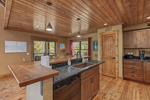 A kitchen with wooden cabinets, a granite countertop, a dishwasher, and a window with a view of trees.