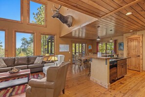 A spacious living area with a large window, a wooden ceiling, and a mounted deer head.