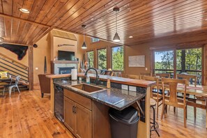 A spacious kitchen with a central island, wooden flooring, and large windows offering views of the outdoors.