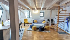 A spacious loft apartment with exposed wooden beams, a loft bed, a sofa set, and a dining area with a table and chairs. - Le Ch'ti Alsacien ***, duplex apartment for 4/6 people in the heart of Eguisheim (Eguisheim)