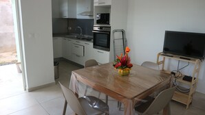 A compact kitchen with a microwave, oven, and sink. There is a dining table with chairs and a small TV stand with a TV.