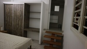 A compact room with a bed, a wardrobe, a small table, and a bathroom with a sink and mirror.