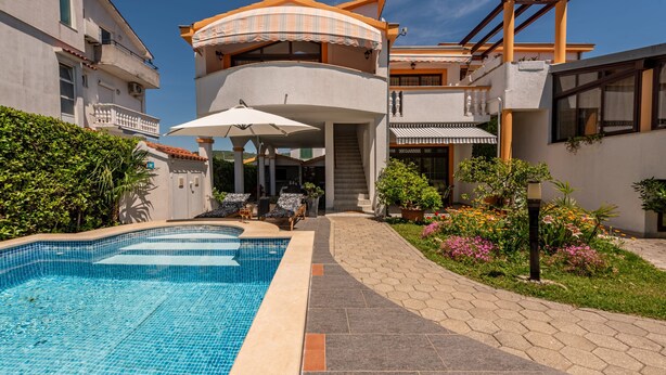 Ett modernt hus i två våningar med en swimmingpool, en uteplats och en trädgård.