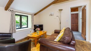 A living room with a wooden table, leather sofa, and a TV. - Stables Cottage - deep in the Devon countryside (Holsworthy)