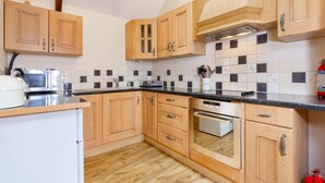 A kitchen with wooden cabinets, a microwave, a toaster, and a tiled backsplash. - Stables Cottage - deep in the Devon countryside (Holsworthy)