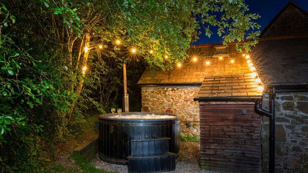 A hot tub surrounded by greenery, with string lights above. - Stables Cottage - deep in the Devon countryside (Holsworthy)