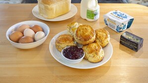 A breakfast setting with eggs, scones, jam, butter, and milk in front of a stone fireplace with a wood stove. - Appleloft Suite in 17th century Farmhouse (Holsworthy)
