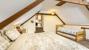 A bedroom with a sloped ceiling, a large bed with patterned bedding, a wooden headboard, and a small bedside table with a lamp. - Appleloft Suite in 17th century Farmhouse (Holsworthy)