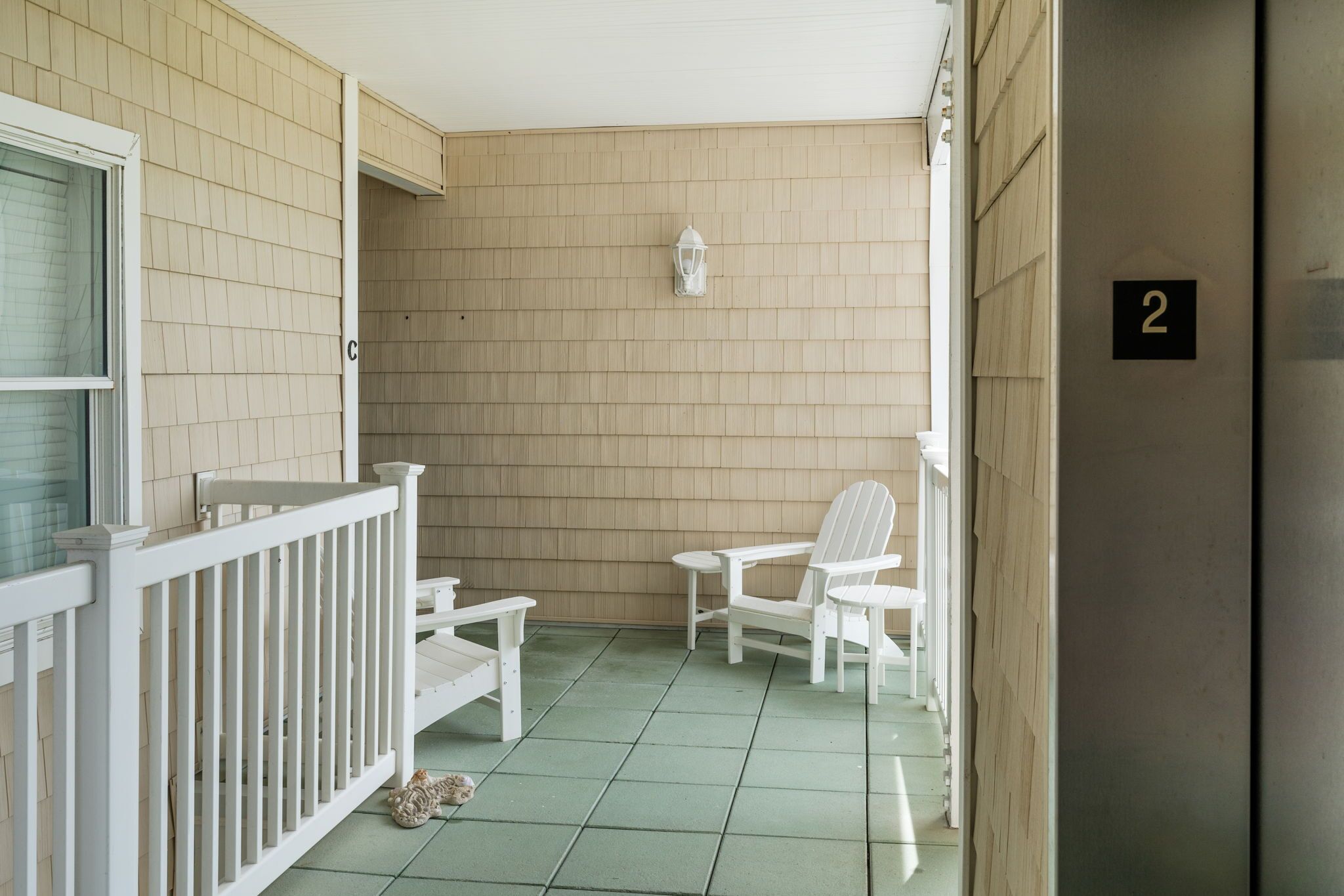 A small porch with a white railing, a white chair, and a small table. A white lantern hangs on the wall.
