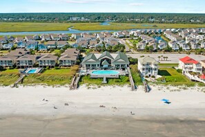 Un quartier résidentiel situé sur la côte, avec une grande maison dotée d’une piscine, entourée d’autres maisons et d’une plage.