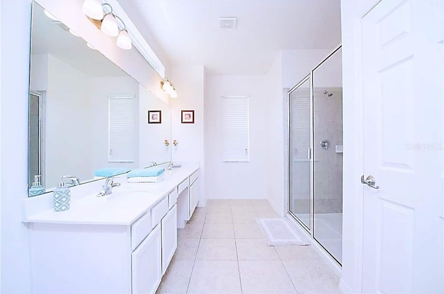 A modern bathroom with a large mirror, two sinks, and a glass-enclosed shower.