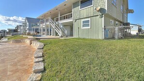 A modern multi-story house with a covered patio, a stone retaining wall, and a well-maintained lawn.