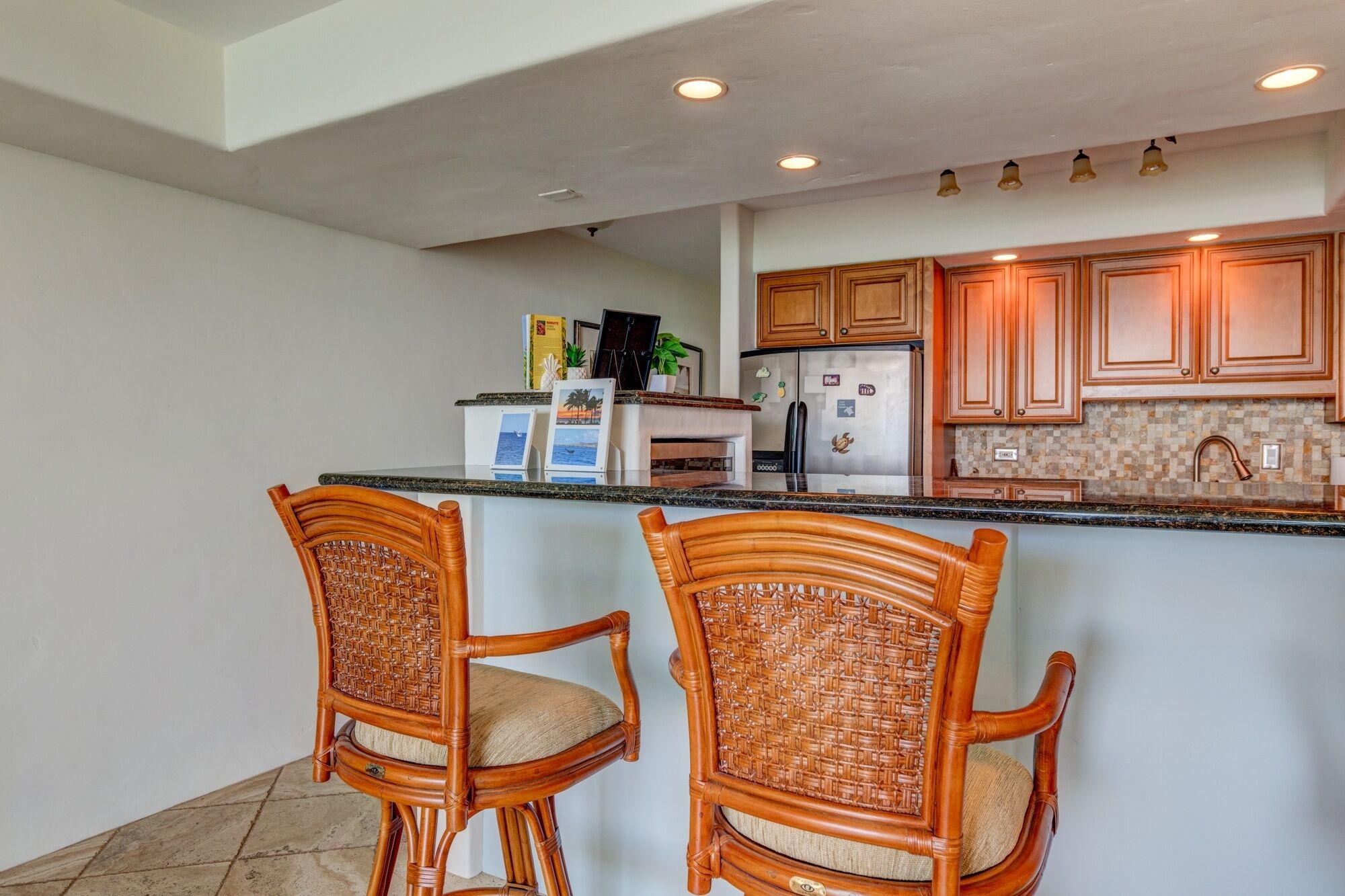A kitchen with wooden cabinets, a refrigerator, and two wicker chairs.