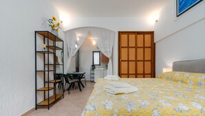 Un dormitorio con cama, escritorio, silla, armario y una estantería con un jarrón de flores.