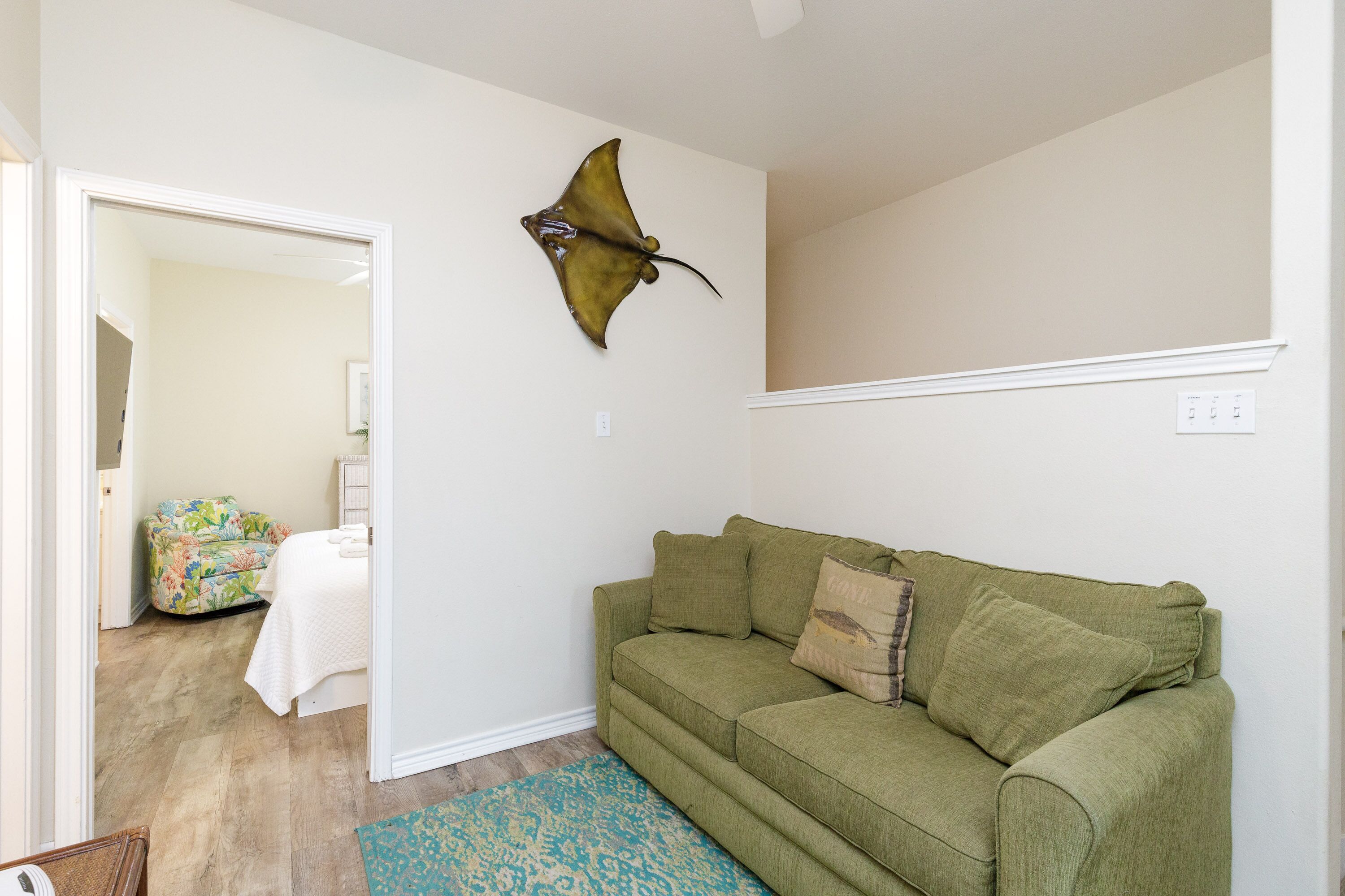 Une pièce avec un canapé vert, un tapis à motifs et un objet décoratif fixé au mur.