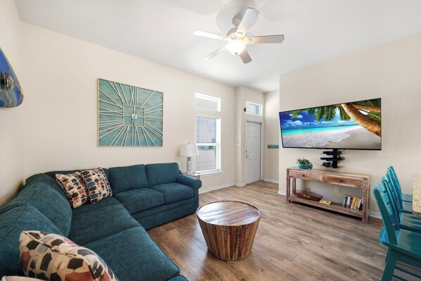 A living room with a sectional sofa, a round coffee table, a television on a wooden stand, and a painting on the wall.