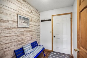 A room with a wooden wall, a white door, a bench, and a framed picture.