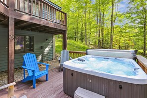 Ein Whirlpool auf einer Holzterrasse mit einem blauen Stuhl, umgeben von einem Wald.