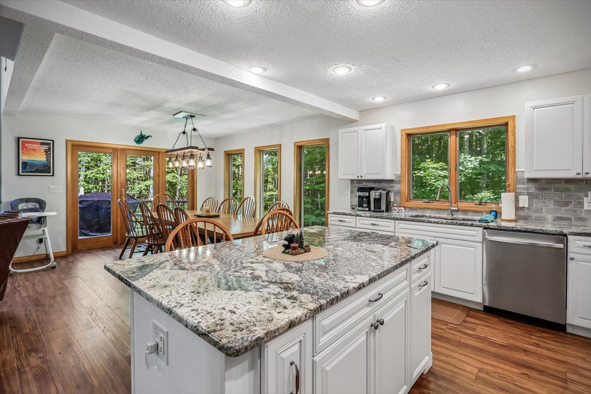 A modern kitchen with white cabinets, granite countertops, and a dining area with wooden chairs.