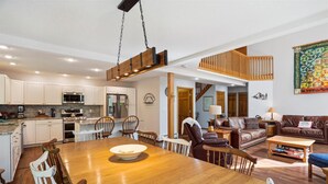 Ein großzügiger Wohnbereich mit Esstisch aus Holz, Ledersofas und einer Küche mit weißen Schränken und modernen Geräten.