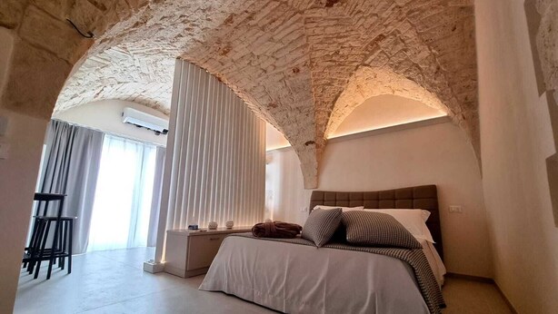 Une chambre avec un plafond en pierre, un lit avec une literie blanche, une table de chevet et une chaise.