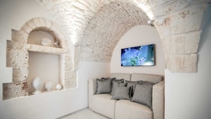 Une pièce avec une arche en pierre, un canapé avec des coussins gris et un téléviseur fixé au mur.