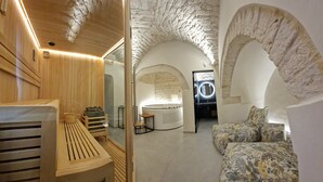 Une salle de spa avec un banc en bois, une table de massage, un fauteuil de massage et un mur en pierre.