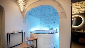 Une salle de bain moderne avec un mur en pierre, une baignoire ronde et un petit tabouret en bois.