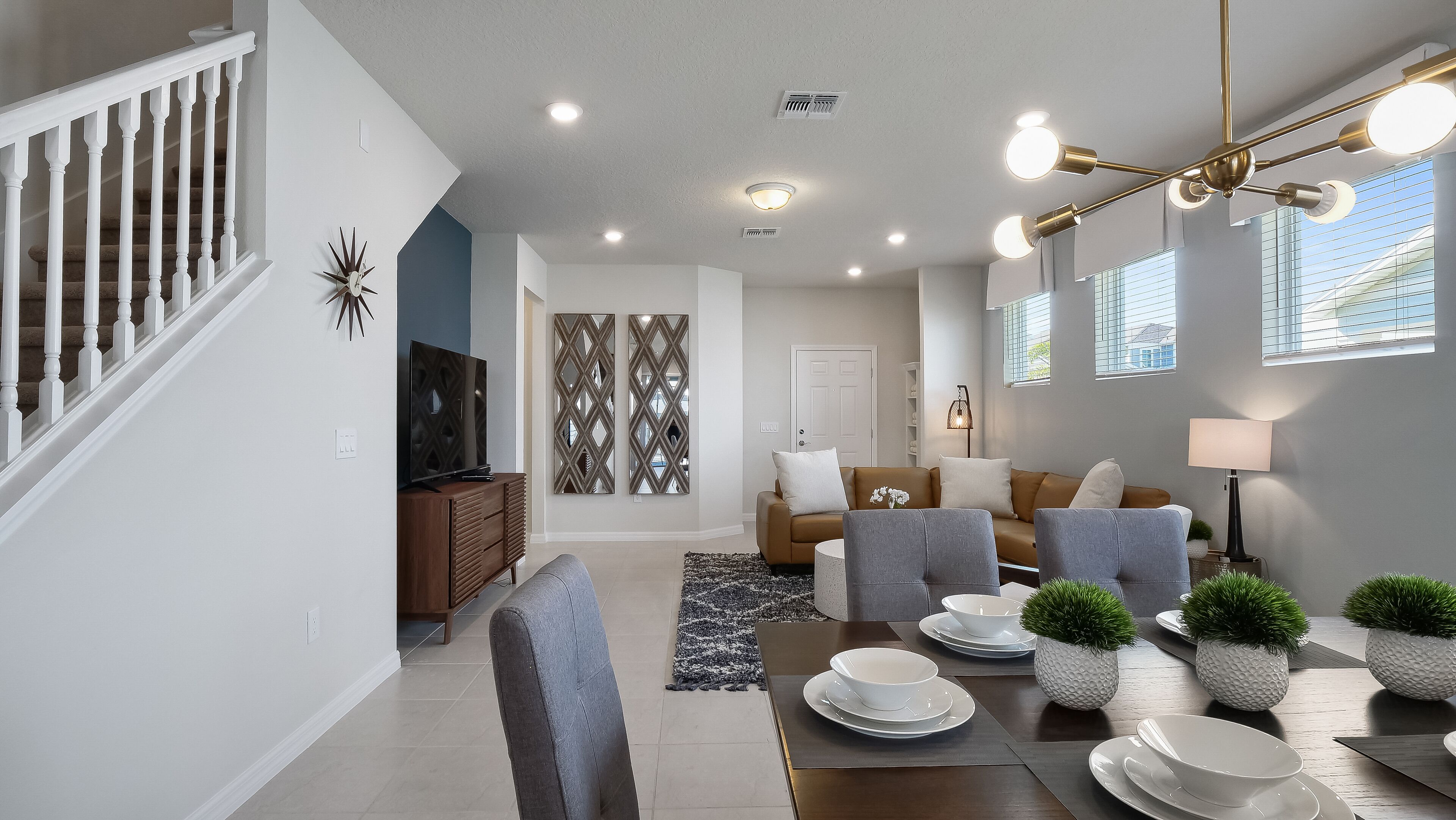 Una sala moderna con una escalera, un televisor de pantalla plana, un conjunto de sofás, una mesa de comedor con platos y tazones, y paneles decorativos en la pared.