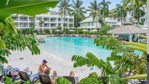 A resort pool area with palm trees, lounge chairs, and a building in the background. - Beach Club Top Floor Spa Suite 3131 (Palm Cove)