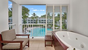 A balcony with a view of a swimming pool, a wooden bench, a small table, and a large bathtub. - Beach Club Top Floor Spa Suite 3131 (Palm Cove)