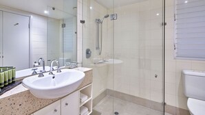 A modern bathroom with a large mirror, a sink, a shower, and a toilet. - Beach Club Top Floor Spa Suite 3131 (Palm Cove)