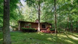 A wooden cabin with a porch, surrounded by a forested area. - Mid-Century Gem • Creekside • King Beds • Near UNC (Chapel Hill)