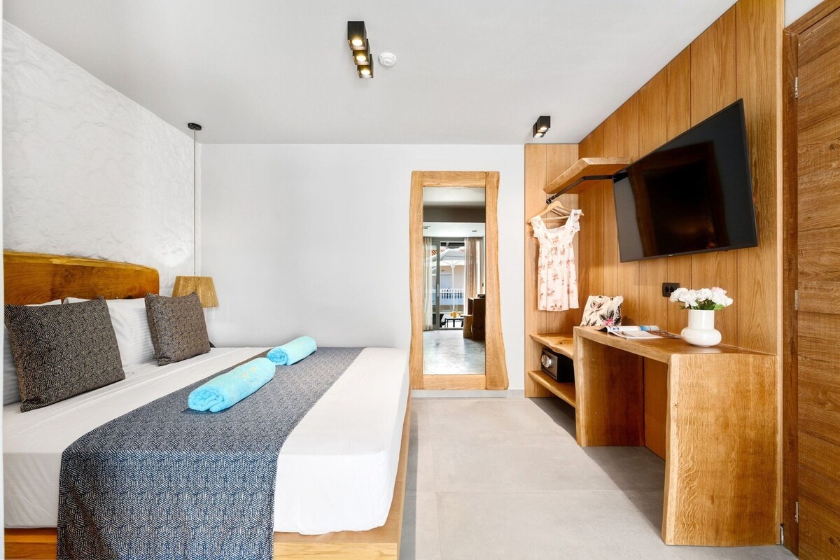 A modern hotel room with a bed, a desk with a flat-screen TV, and a wooden wardrobe.