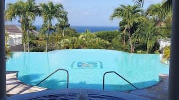 Vista a través de un arco de una piscina con una fuente, rodeada de palmeras y un cielo despejado.