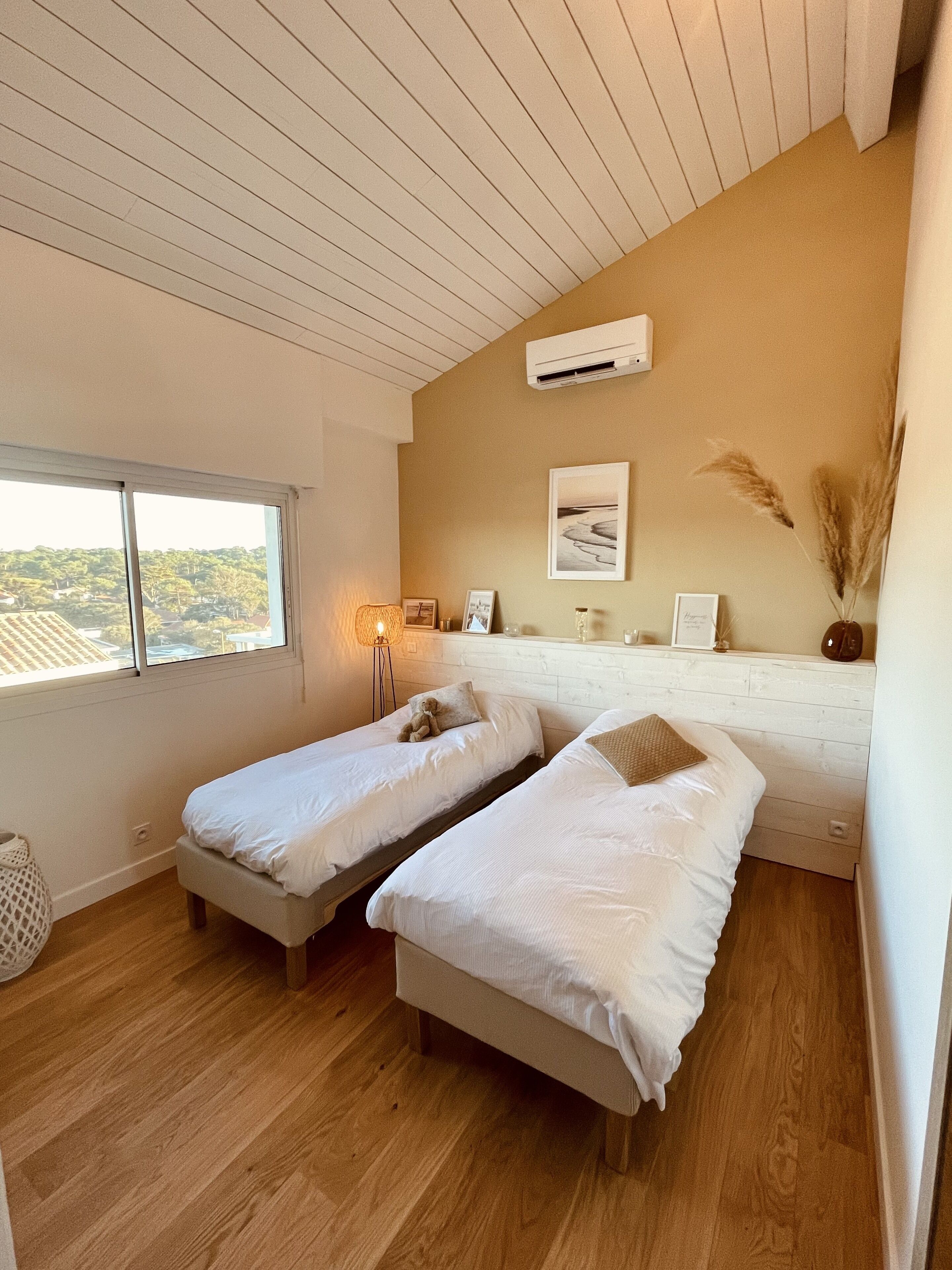 Une chambre avec deux lits simples, une fenêtre donnant sur un paysage agréable, un climatiseur fixé au mur et une lampe de chevet.