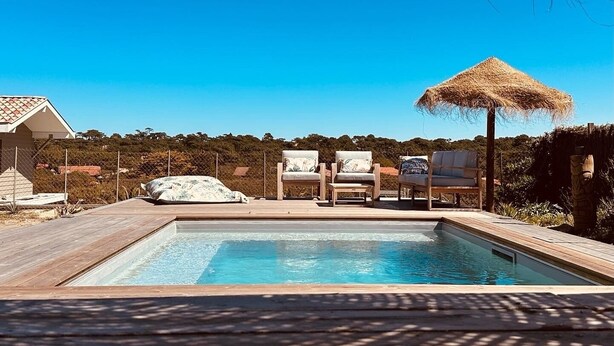 A swimming pool with a wooden deck, lounge chairs, and a thatched umbrella. - "La Villa Tchanquée " Dominant view of the Ocean & Pines (Soorts-Hossegor)