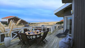 A wooden deck with a table and chairs, overlooking a beach and a distant building. - "La Villa Tchanquée " Dominant view of the Ocean & Pines (Soorts-Hossegor)