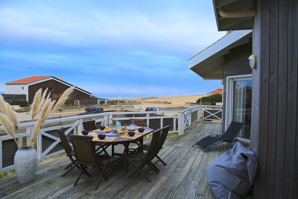 A wooden deck with a table set for dining, overlooking a beach. - "La Villa Tchanquée " Dominant view of the Ocean & Pines (Soorts-Hossegor)