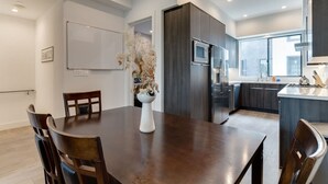 A modern kitchen with dark cabinetry, a stainless steel refrigerator, and a dining area with a wooden table and chairs. - Modern 4 Bedroom Charmer w/ Rooftop Deck House #2  (Los Angeles)