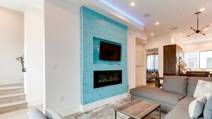 A modern living room with a large gray sectional sofa, a coffee table, and a blue accent wall with a TV and fireplace. - Modern 4 Bedroom Charmer w/ Rooftop Deck House #2  (Los Angeles)