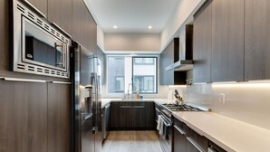 A modern kitchen with dark wood cabinets, stainless steel appliances, and a large window providing natural light. - Modern 4 Bedroom Charmer w/ Rooftop Deck House #2  (Los Angeles)